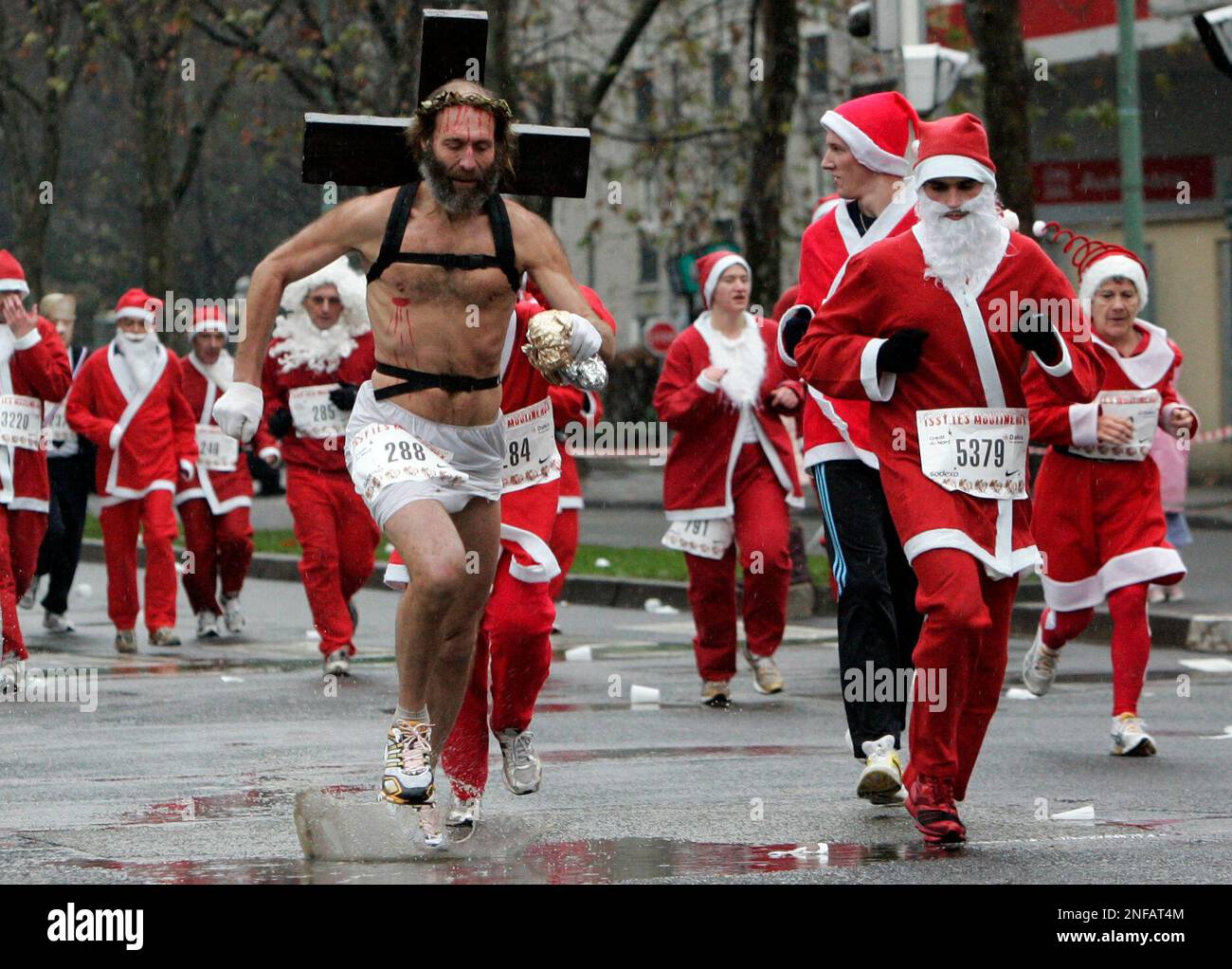 Runners, dressed as Santa Claus, one of them carrying a cross on his shoulders to resemble Jesus Christ, take part of the "Christmas Corrida Race" in the streets of Issy Les Moulineaux, west outskirts of Paris, Sunday, Dec. 14, 2008. (AP Photo / Francois Mori) Banque D'Images