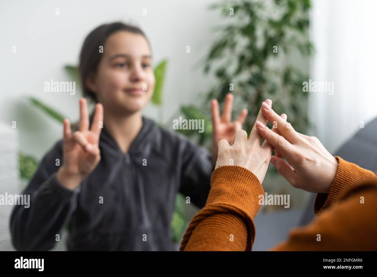 la fille parle avec des mères d'âge moyen en utilisant la langue des signes, la famille assise sur le côté du fauteuil vue, enseignant enseigner à l'adolescent sourd-muet fille à Banque D'Images