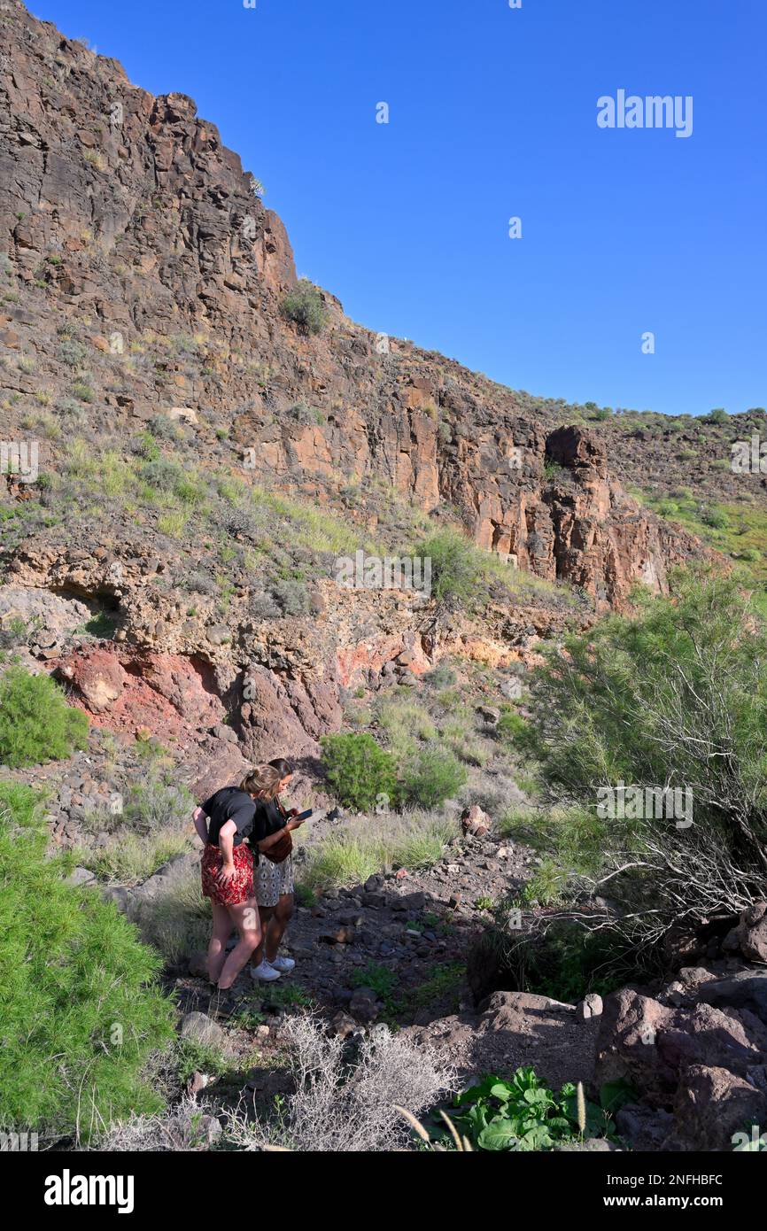 Deux jeunes femmes qui se sont inscrites au téléphone dans un paysage de montagne rocailleux dans la gorge « Barranco de las Vacas », dans les montagnes près d'Aguimes, Gran Canaria Banque D'Images Deux jeunes femmes qui se sont inscrites au téléphone dans un paysage de montagne rocailleux dans la gorge « Barranco de las Vacas », dans les montagnes près d'Aguimes, Gran Canaria Banque D'Images