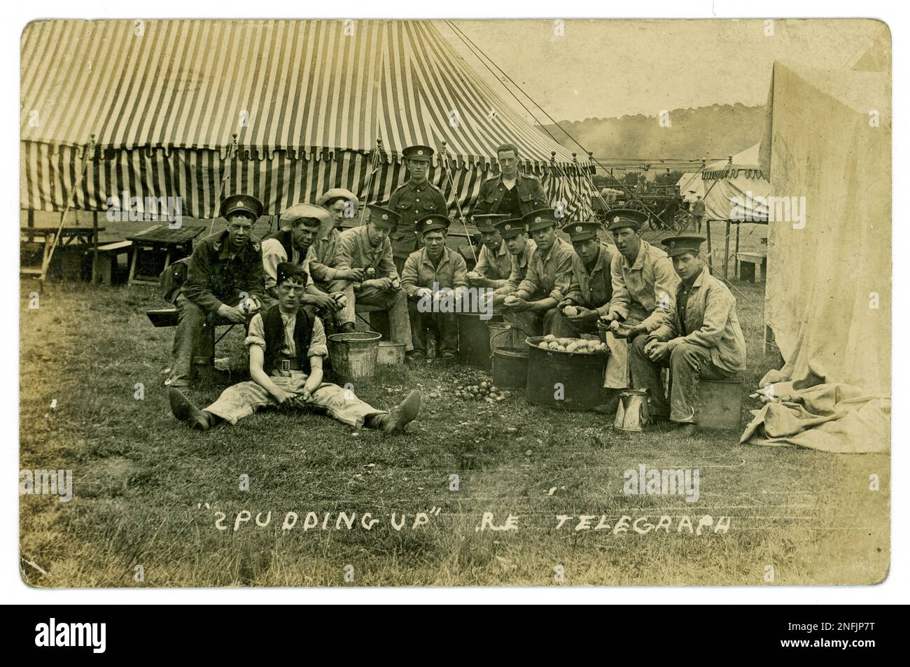 Carte postale WW1 du groupe des Royal Engineers du Telegraph corps, pelant les pommes de terre à côté de la tente du camp, intitulée « Pudding Up R.E. Telegraph ». Trois des hommes ont le corps territorial du Lincolnshire visible et le reste est probablement le même, mais leur uniforme est recouvert d'un blouson de travail. Un camion d'approvisionnement est à l'arrière-plan regardé par des civils. Vers 1915, peut-être un camp d'entraînement dans le Lincolnshire, au Royaume-Uni Banque D'Images