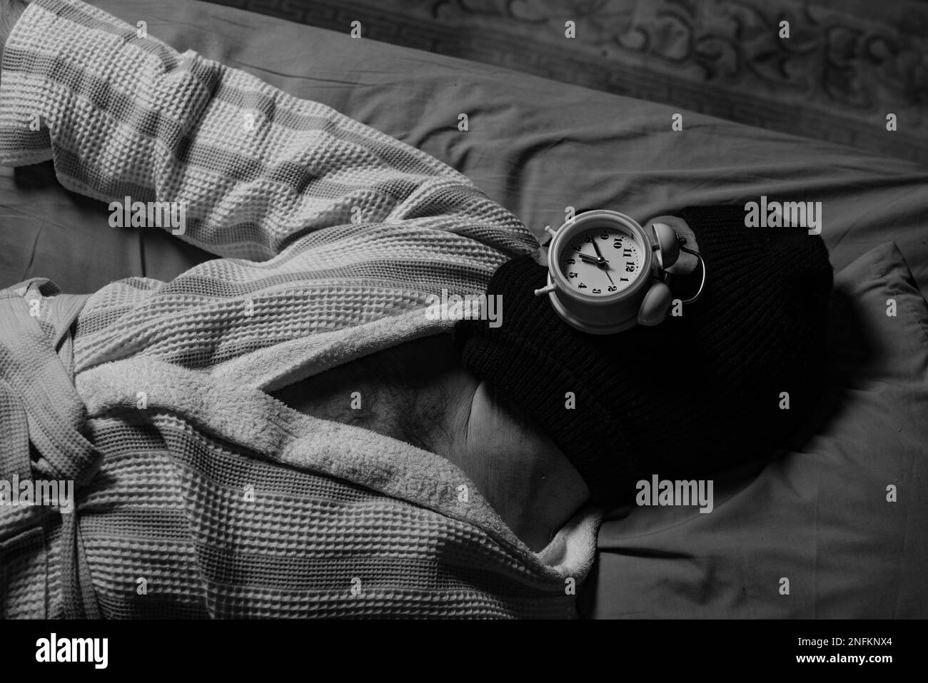 Voleur de temps, concept de procrastination. Un homme dans une balaclava se trouve et dort avec un réveil sur son visage. Gérez votre temps. Image en noir et blanc. Banque D'Images