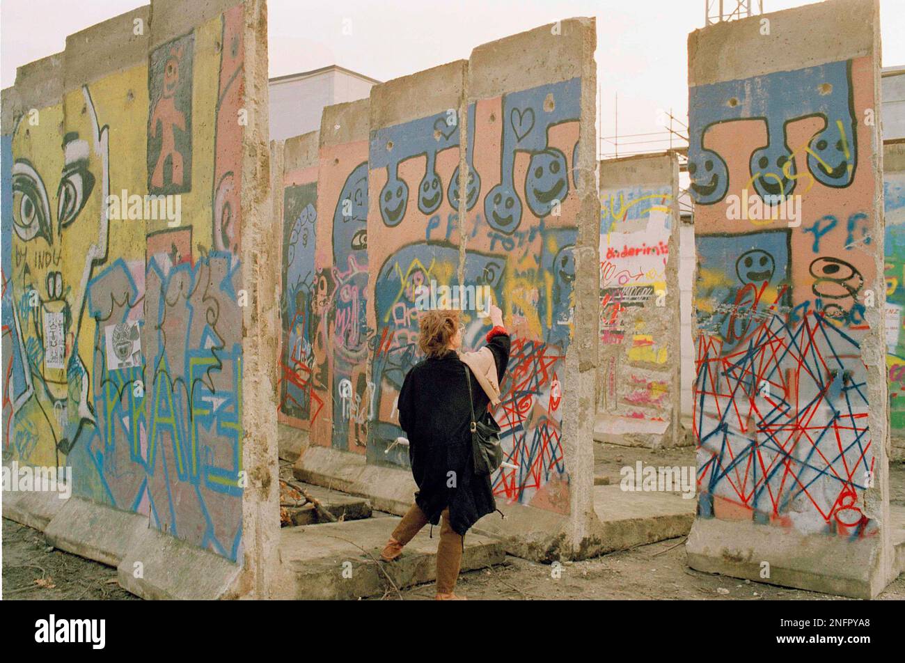 A visitor looks at graffiti splattered segments of the former Berlin Wall, in East Berlin, Jan. 25, 1990. The sections, taken out of the wall in the Kreuzberg district earlier, are stored here to be inspected and sold to the bidders from all over the world. The income will be used to sponsor aid programs in East Germany. (AP Photo/Roland Weihrauch) Banque D'Images