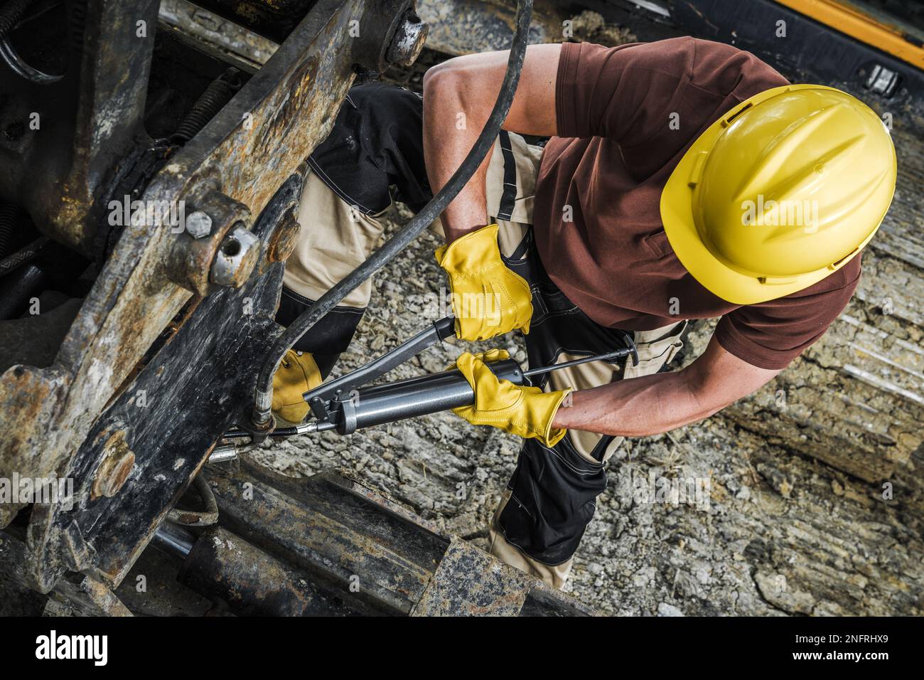 Un technicien en machinerie lourde pompe de la graisse dans la machine industrielle à l'aide d'un pistolet à pompe manuel. Vue de dessus. Banque D'Images