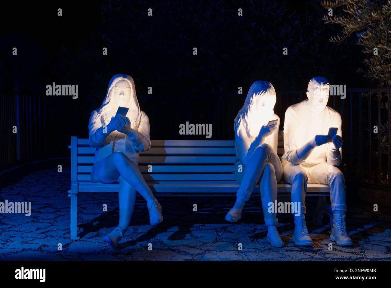 Brescia - Italie. 15 février 2023: La lumière est la vie, (Festa delle Luci A2A), des figures humaines illuminées tenant des téléphones mobiles et assis sur un banc Banque D'Images