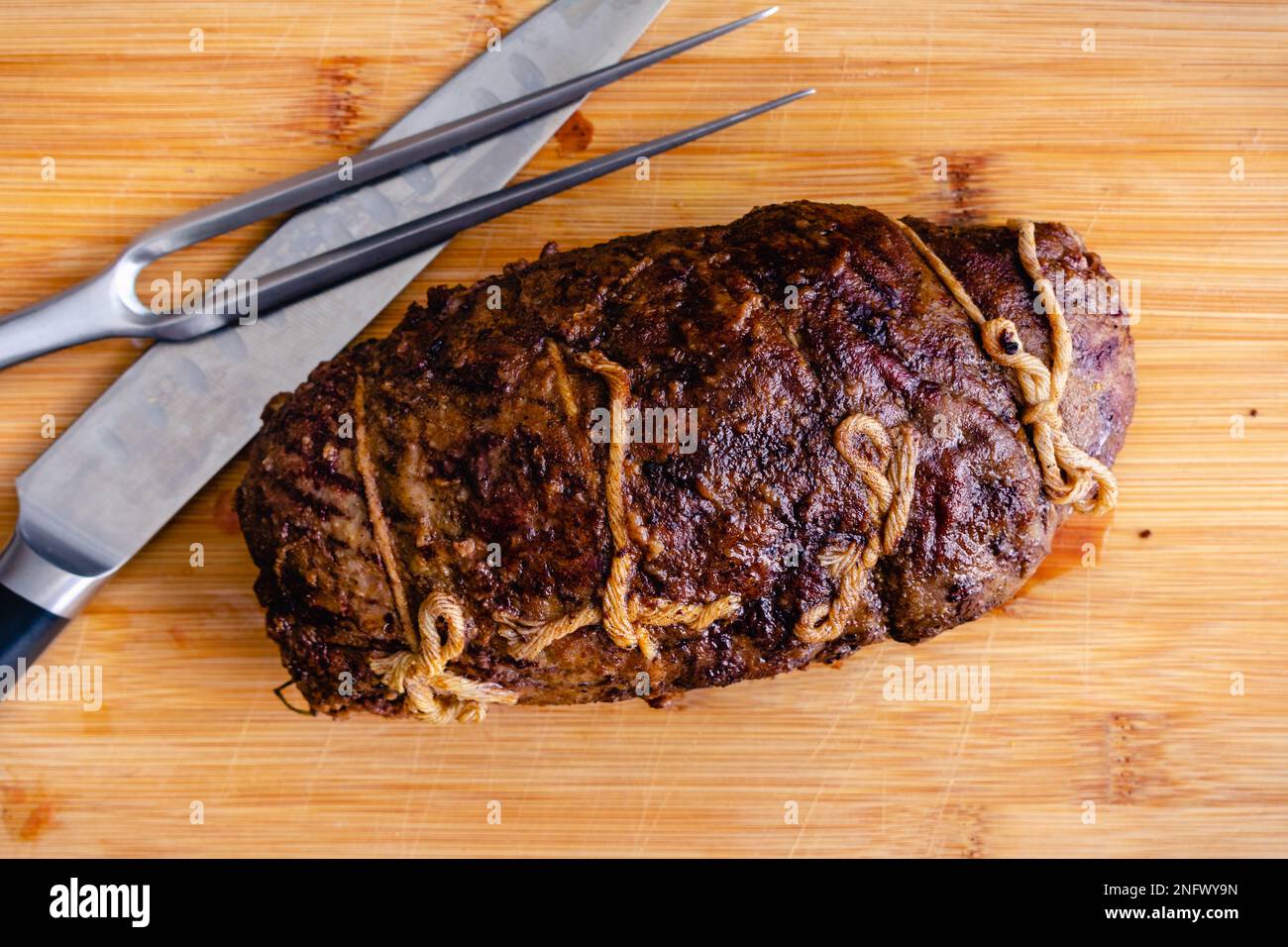 Steak de bœuf entier farci au prosciutto et aux champignons au plafond : roulade de steak non tranché sur une planche à découper avec un couteau à découper et une fourchette Banque D'Images