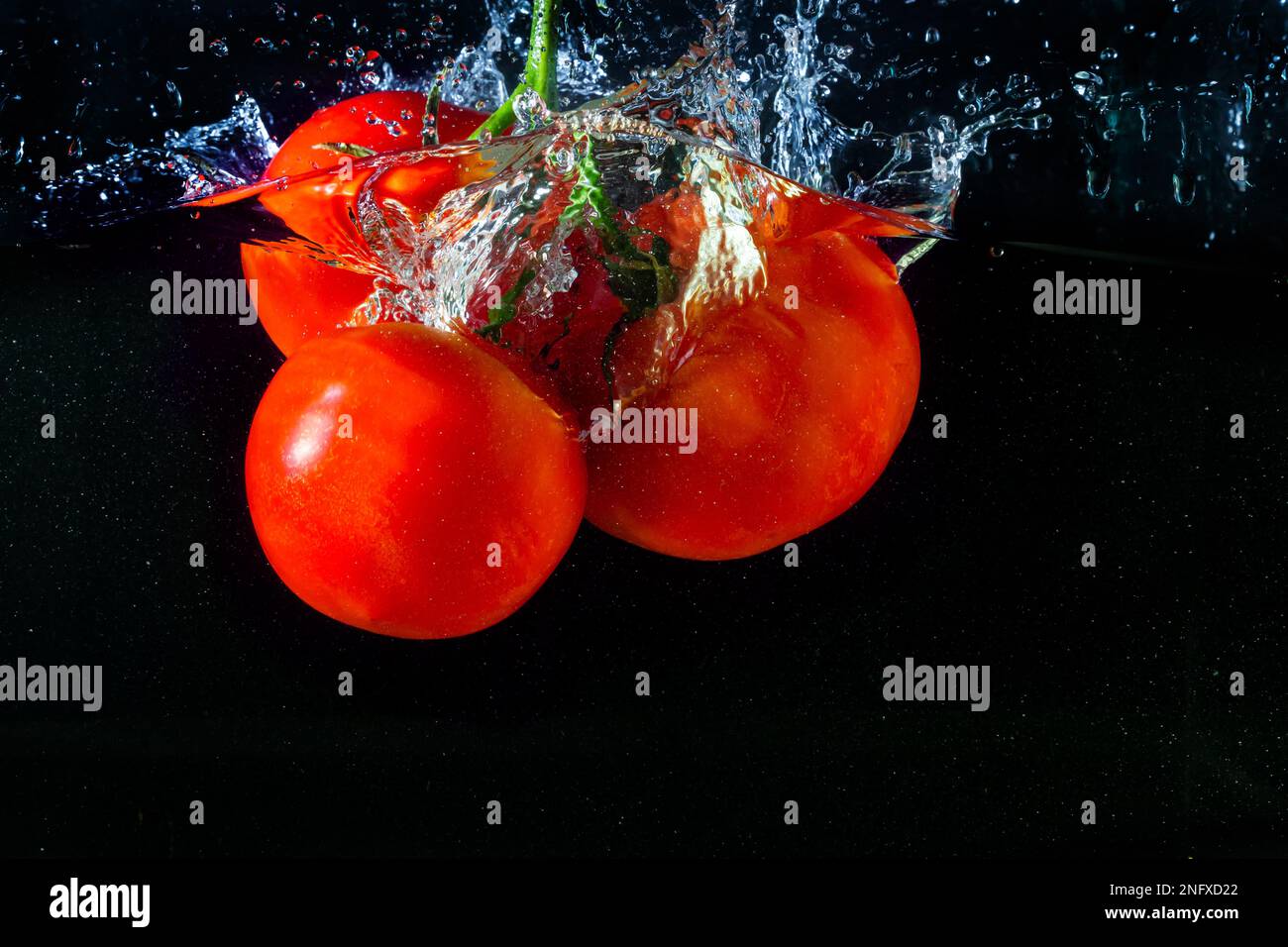 Tomate rouge fraîche tombant dans l'eau avec des éclaboussures d'eau et des bulles d'air isolées sur fond noir. Banque D'Images