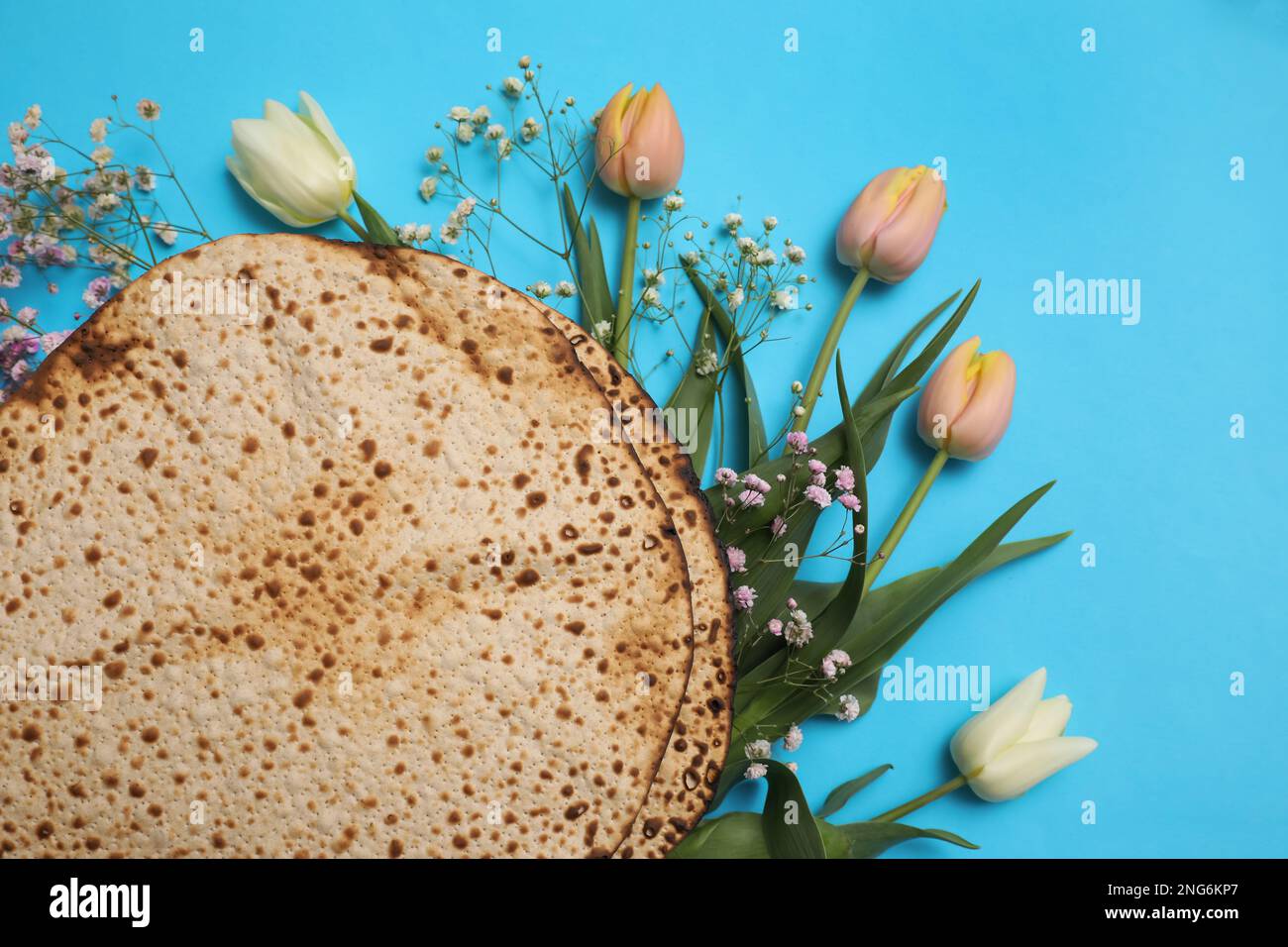 Savoureux matzos et fleurs fraîches sur fond bleu clair, plat. Fête de la Pâque (Pesach) Banque D'Images