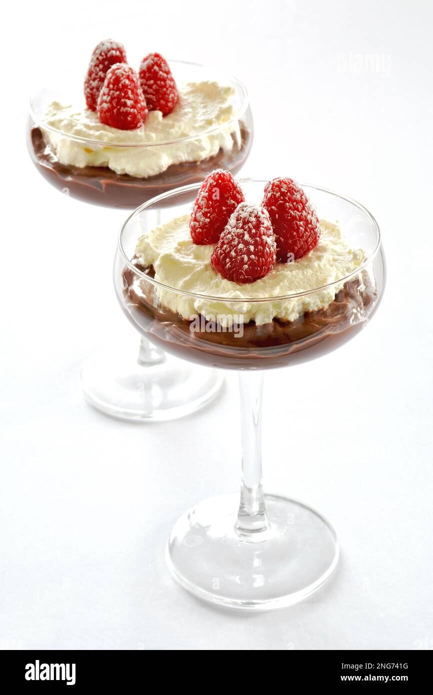 Dessert crème fouettée à la framboise au chocolat dans d'élégantes lunettes de coupe au format vertical. Fruits frais, crème décadente et pudding au chocolat. Banque D'Images