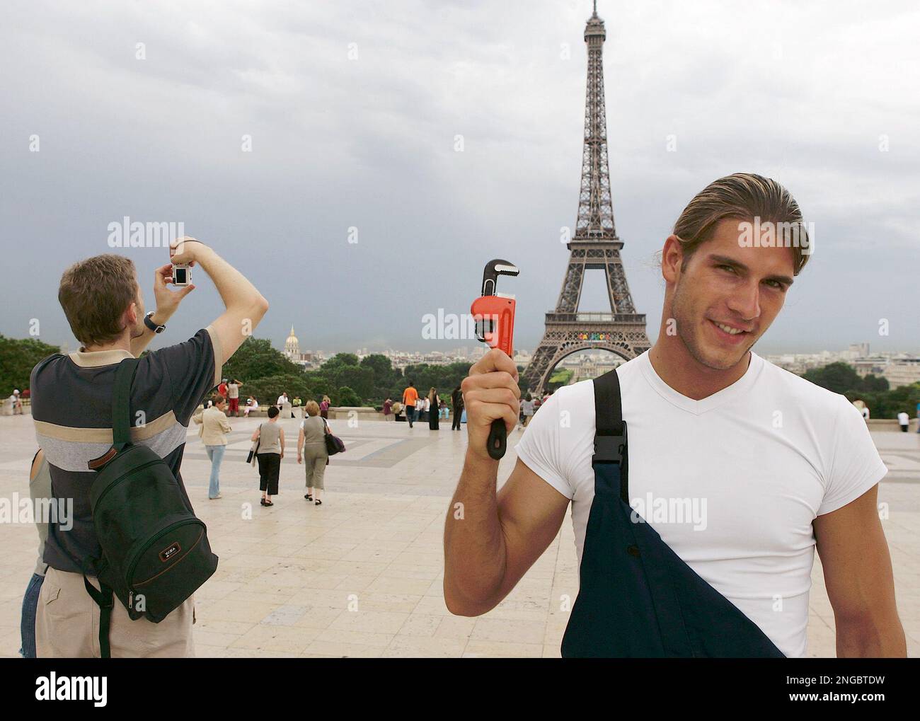 Polish model Piotr Adamski shows a wrench as he poses next to tourists in front of the Eiffel Tower in Paris, Tuesday, June 28, 2005. Adamski acted as a Polish plumber, the frightening symbol of cheap labor in France. The muscled, square-jawed plumber as portrayed in a smart ad campaign by the polish tourism board held a news conference earlier to welcome the French to Poland. (AP Photo/Francois Mori) Banque D'Images