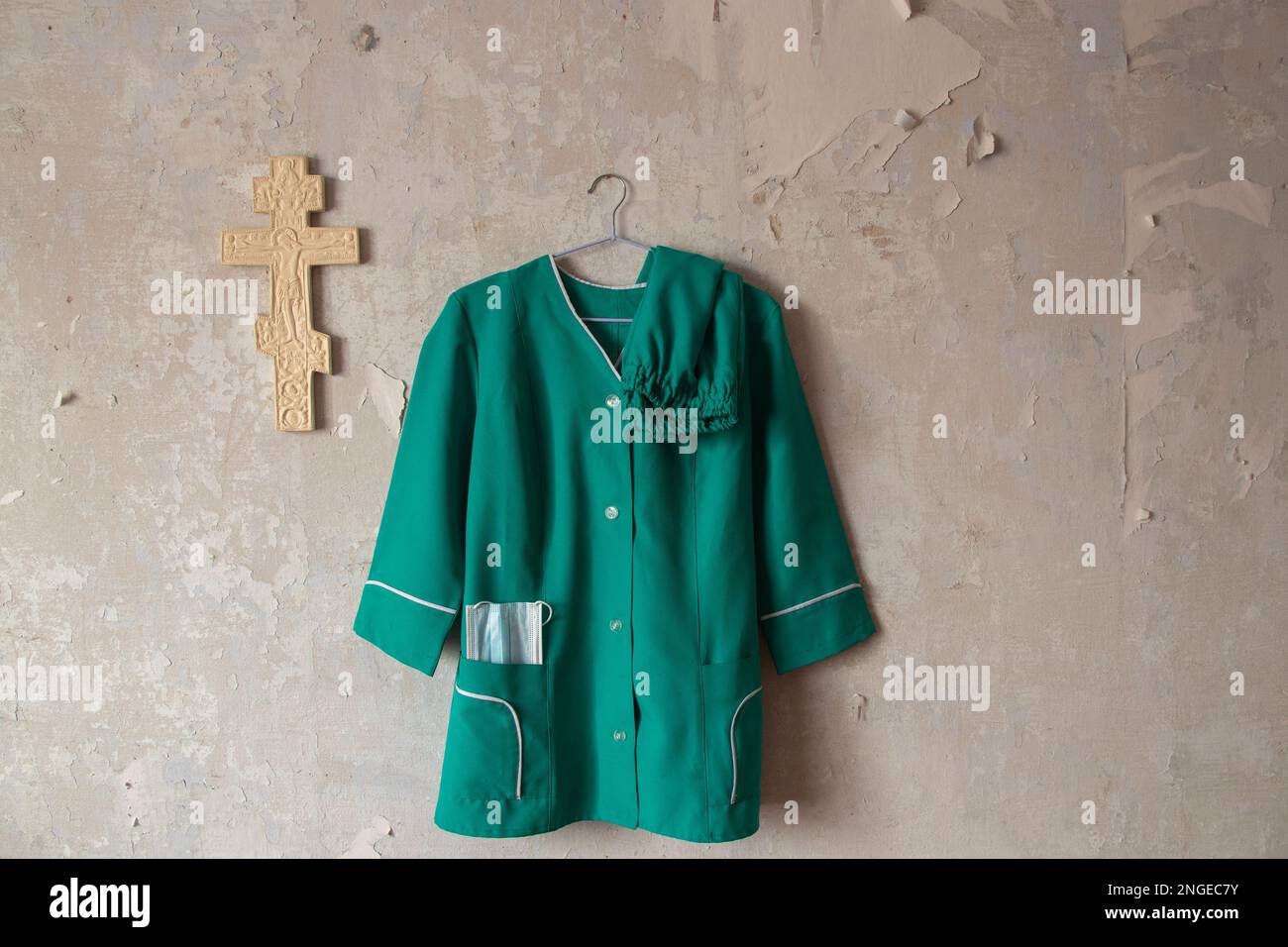 Ukraine costume d'infirmière suspendu sur un vieux mur blanc près d'une croix chrétienne en plâtre à l'intérieur Banque D'Images