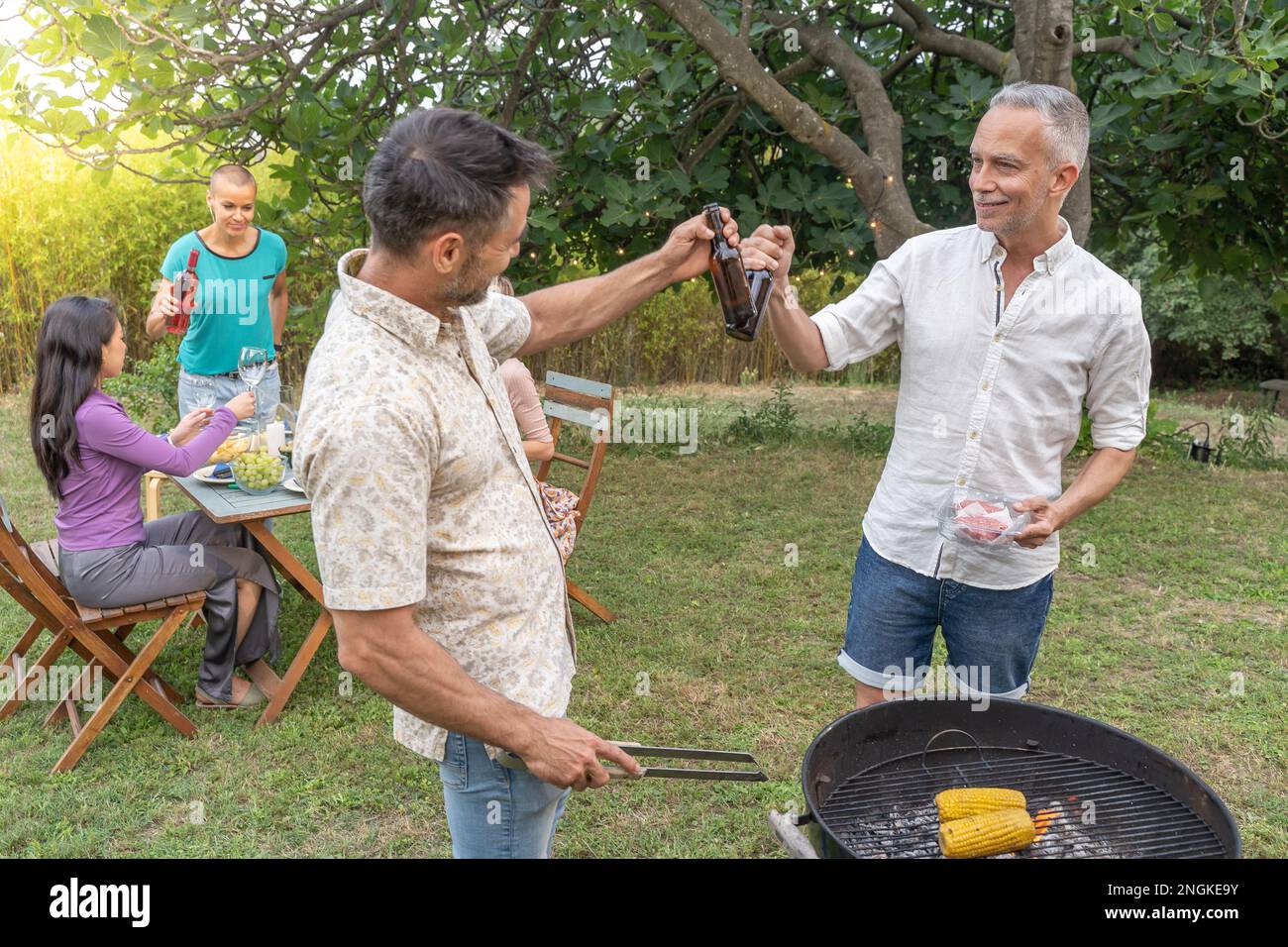 Groupe d'amis qui se font un plaisir de griller autour du barbecue. Des gens souriants buvant sur le patio. Banque D'Images