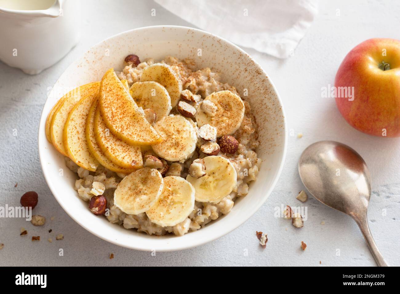 Délicieux petit déjeuner sain. Flocons d'avoine avec banane, pomme, noix et cannelle sur fond gris clair, vue du dessus Banque D'Images