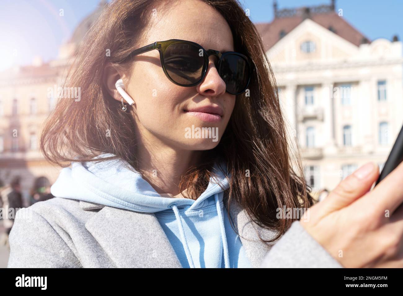 Portrait brune femme avec écouteurs dans des lunettes de soleil debout dans la rue en ville. Banque D'Images