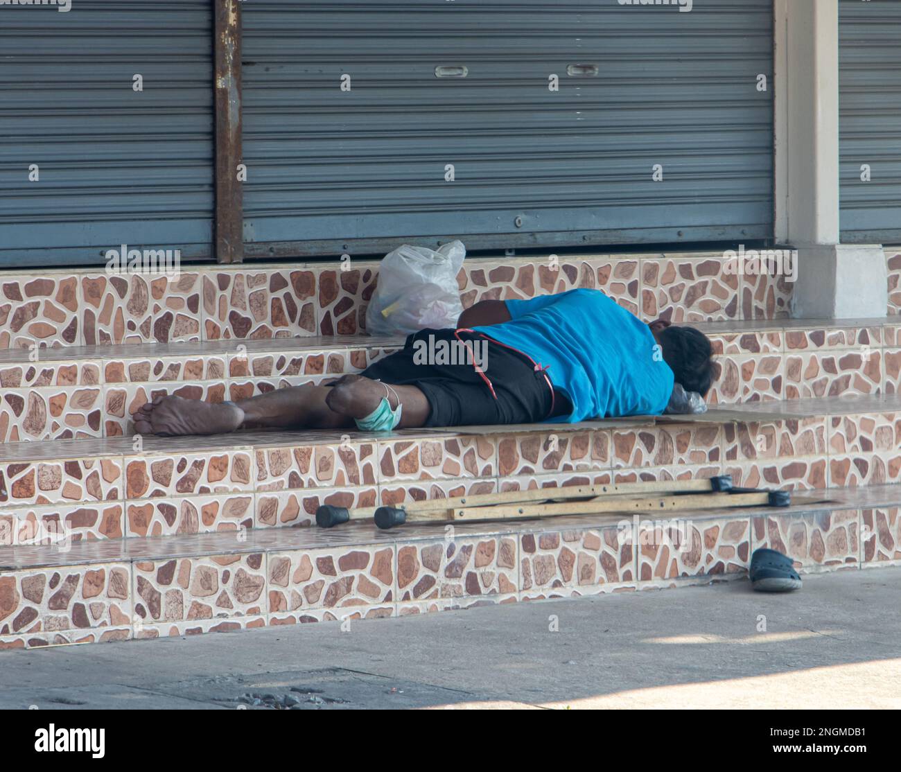 Homme handicapé - invalide, allongé sur les escaliers en face de la porte métallique fermée. Banque D'Images