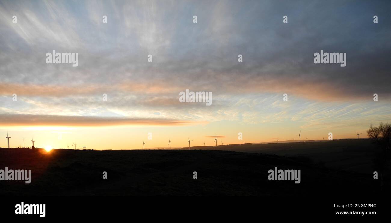 Paysage de coucher du soleil d'hiver à l'horizon avec lumière dorée reflétée dans les nuages et le ciel avec un grand nombre d'éoliennes à distance Banque D'Images