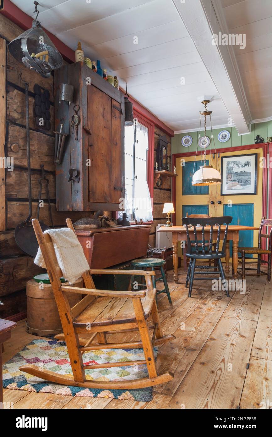 Chaise à bascule ancienne, poêle en fonte avec longue poignée accrochée au mur en bois de pièce, armoires en bois et table en bois de pin dans la vieille maison. Banque D'Images