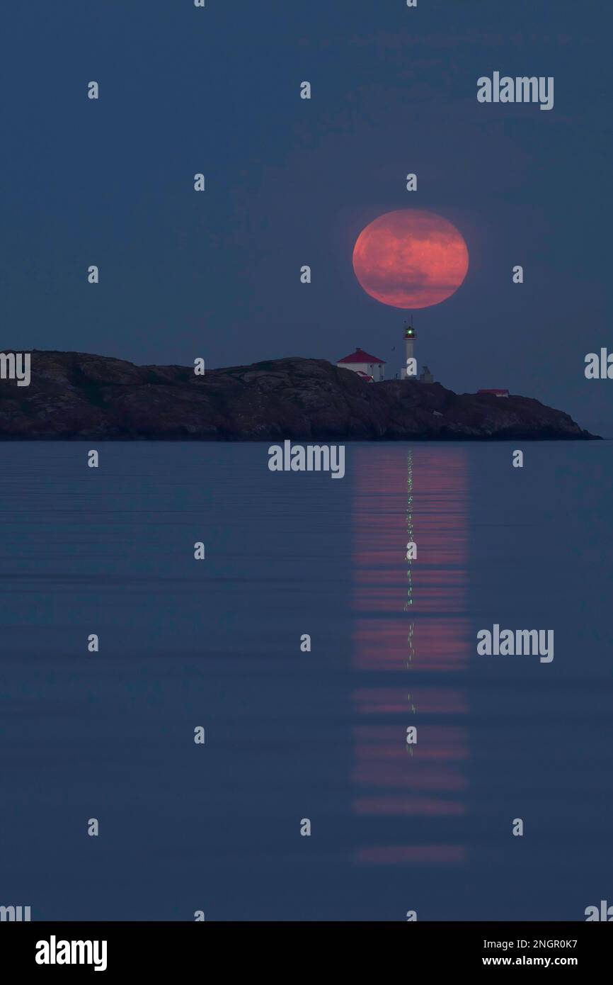 La pleine lune qui s'élève derrière le phare des îles Trial, au large de Victoria, en Colombie-Britannique, au Canada. La lumière du phare se reflète avec la lune dans le Banque D'Images