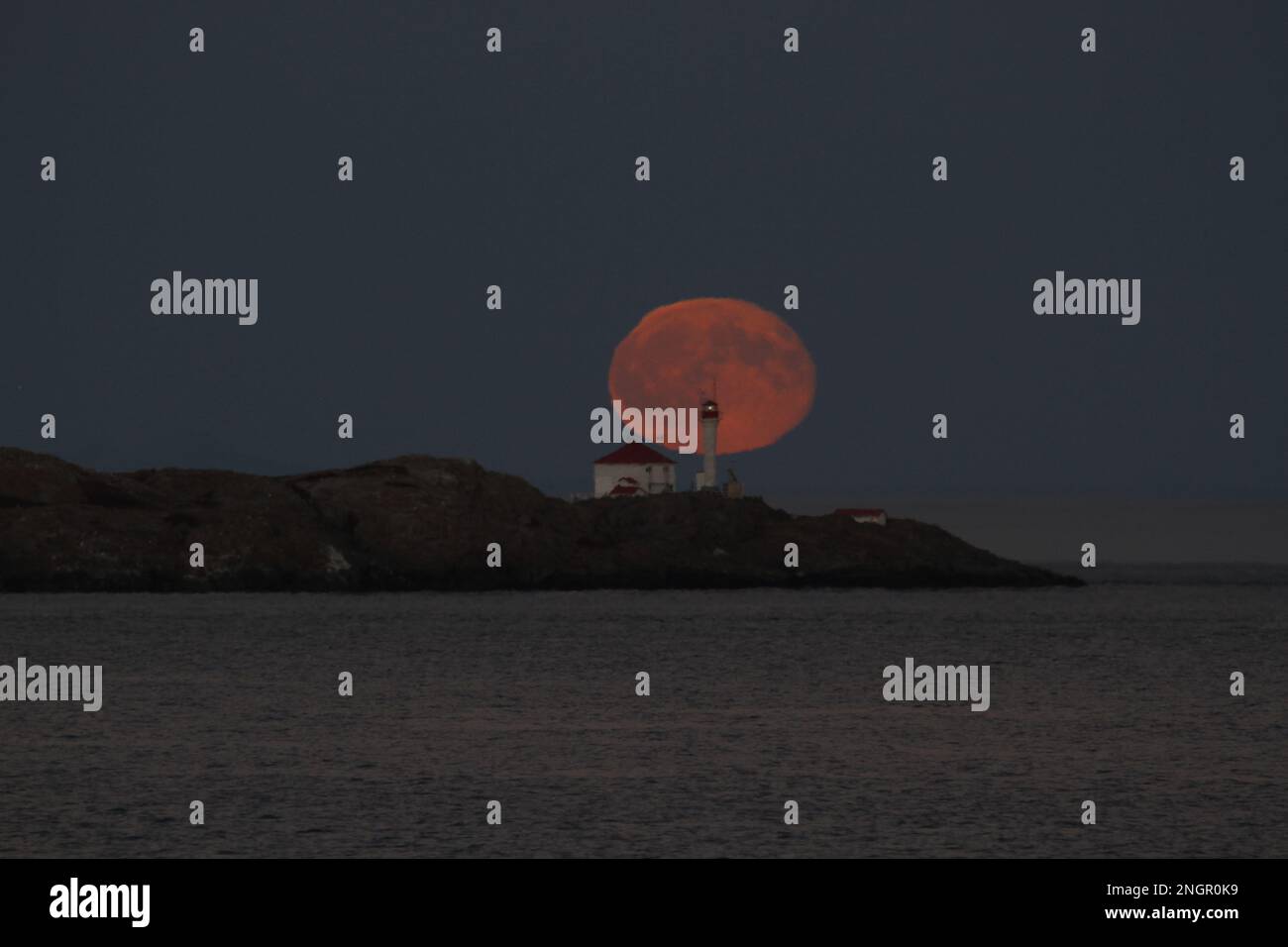 La pleine lune qui s'élève derrière le phare des îles Trial, au large de Victoria, en Colombie-Britannique, au Canada. Banque D'Images