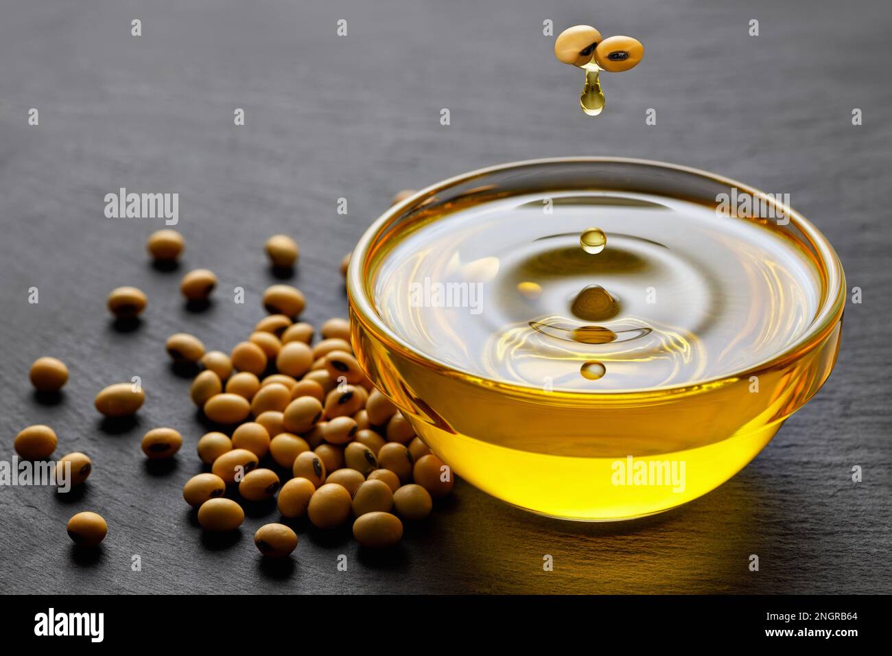 l'huile de soja s'égoutte des haricots dans le bol et des graines de soja sur fond de pierre noire Banque D'Images