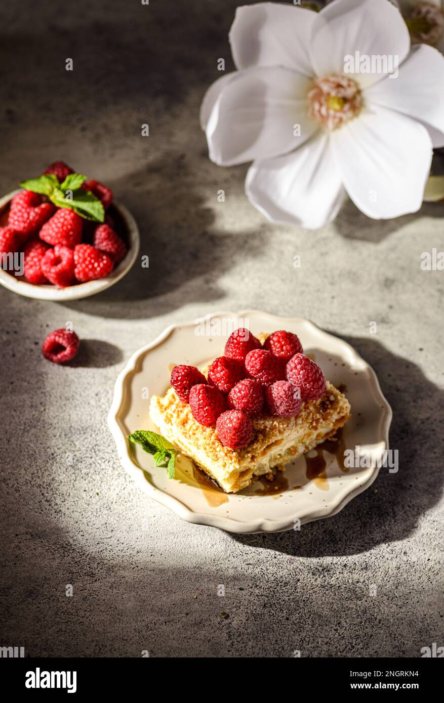 gâteau napoléon sur fond gris. le gâteau est fait de gâteaux de pâte feuilletée à la crème anglaise et décoré avec des framboises fraîches Banque D'Images