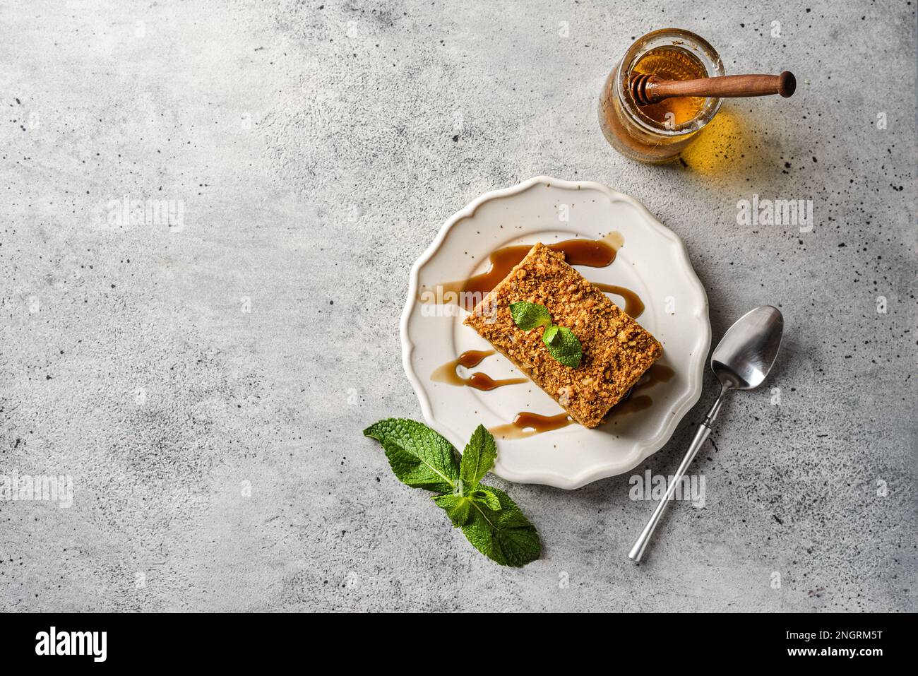 gâteau au miel sur fond gris. Gâteaux au miel et à la crème au beurre, décorés de menthe, à côté d'une cuillère à miel et d'un pot de miel Banque D'Images