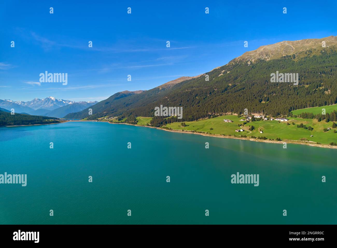 Vue aérienne du lac (Reschensee). Grand réservoir entouré de montagnes à midi ensoleillé. Espace de loisirs pour les touristes et les sportifs. Ferme biologique sur t Banque D'Images
