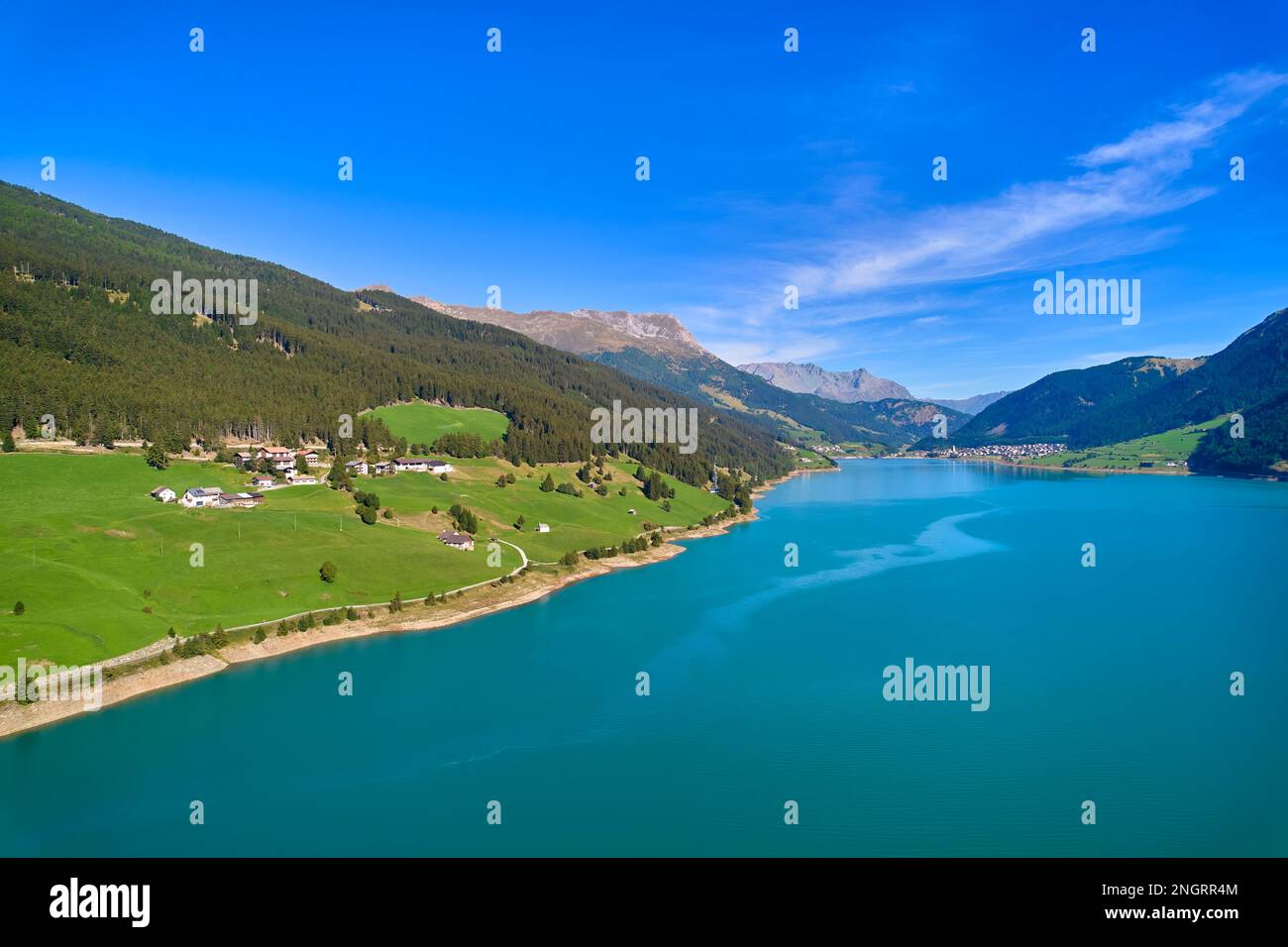Vue aérienne du lac (Reschensee). Grand réservoir entouré de montagnes à midi ensoleillé. Espace de loisirs pour les touristes et les sportifs. Ferme biologique sur t Banque D'Images