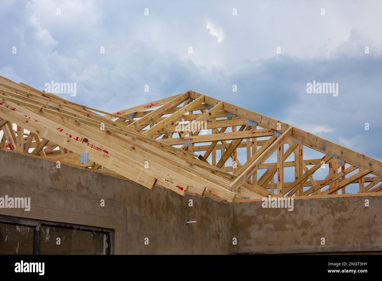 Murs en plâtre non peints et poutres de toit en bois d'une maison en construction avec des nuages orageux en arrière-plan. Banque D'Images