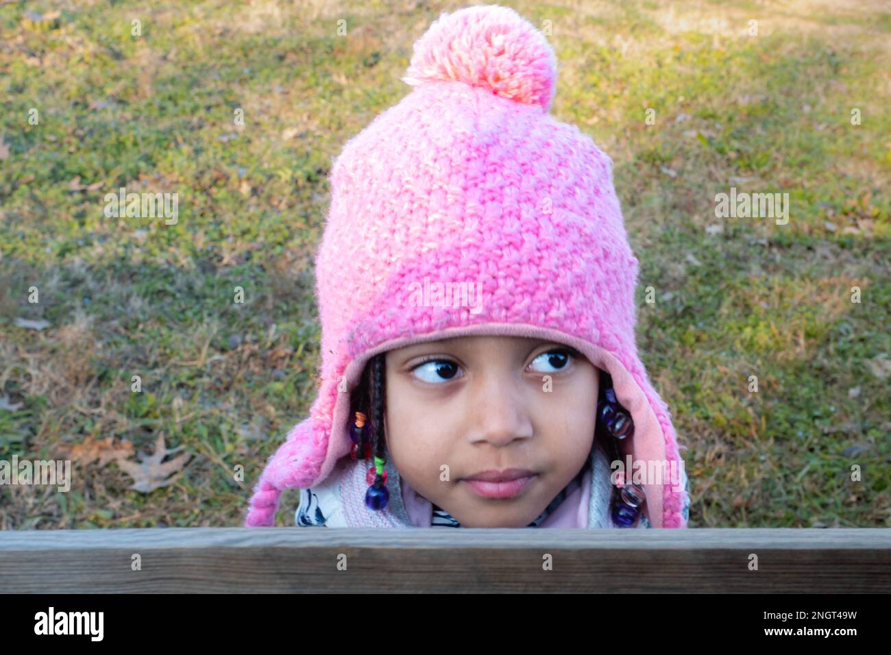 mignon sourire afro-américaine bébé fille en tenue blanche à l'extérieur au coucher du soleil portant un bonnet en tricot beanie rose avec rabats d'oreilles Banque D'Images