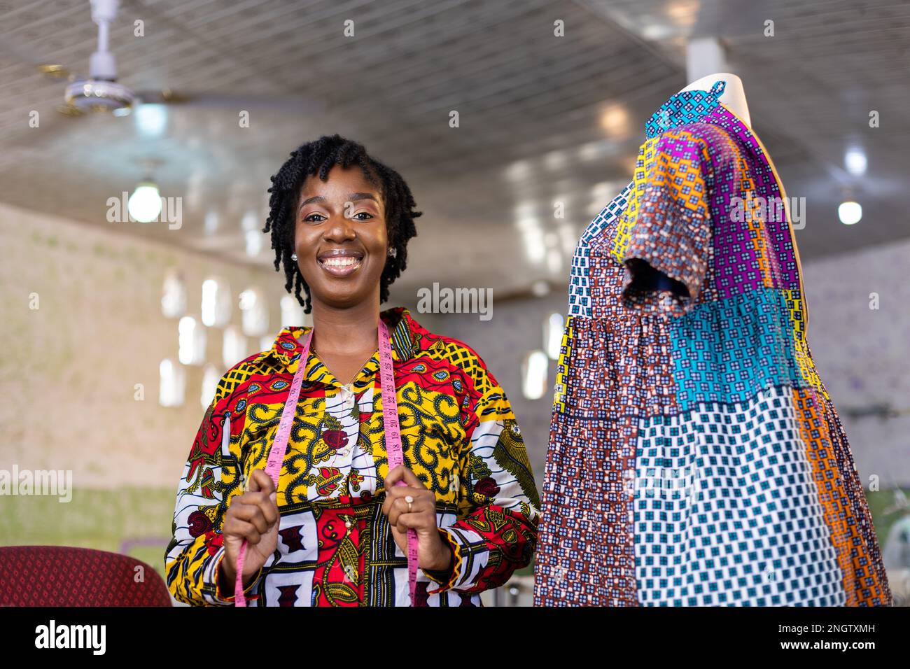 Couturière africaine à succès Entreuner debout par sa robe africaine colorée à motif d'impression avec ruban de mesure autour de son cou. Banque D'Images