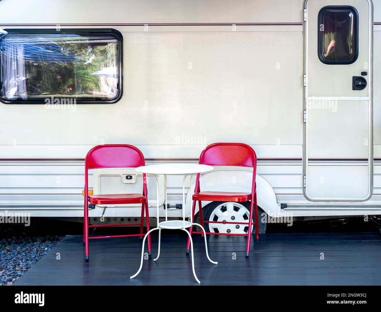 Deux chaises en fer rouge vides avec table ronde blanche devant la porte et la fenêtre de la caravane avec personne. Détente camping et sommeil dans le moteur Banque D'Images