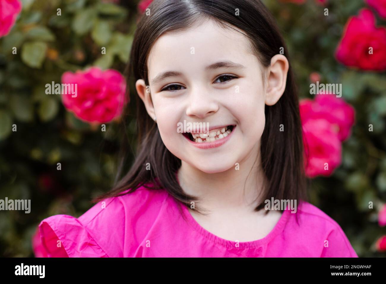 Fille souriante 7-8 ans montrer ses nouvelles dents permanentes dans le sourire dentaire sur la nature fond floral extérieur. Regardez la caméra. Soins de santé. Enfant Banque D'Images