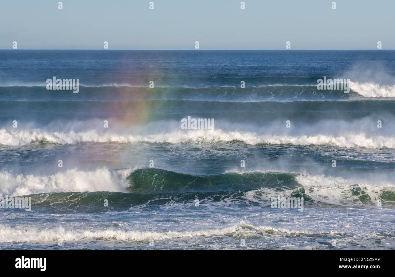 Un arc-en-ciel sur des vagues de surf, formé par la réfraction de la lumière du soleil dans la pulvérisation de l'océan Banque D'Images