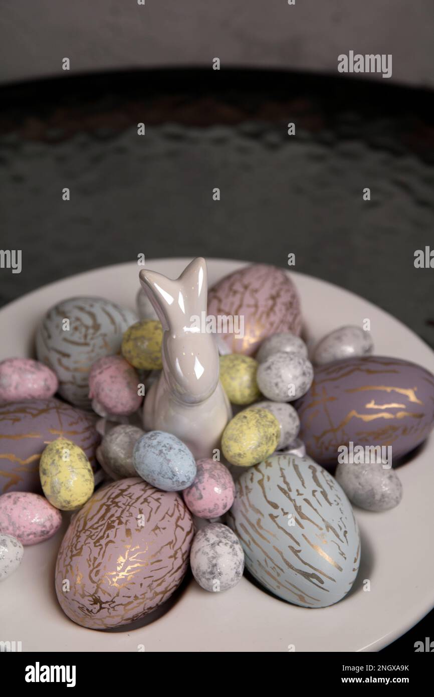 photo de nombreux oeufs de poulet de différentes couleurs et oeufs réagés sur une assiette spéciale pour les oeufs et un lapin décoratif debout sur la table Banque D'Images