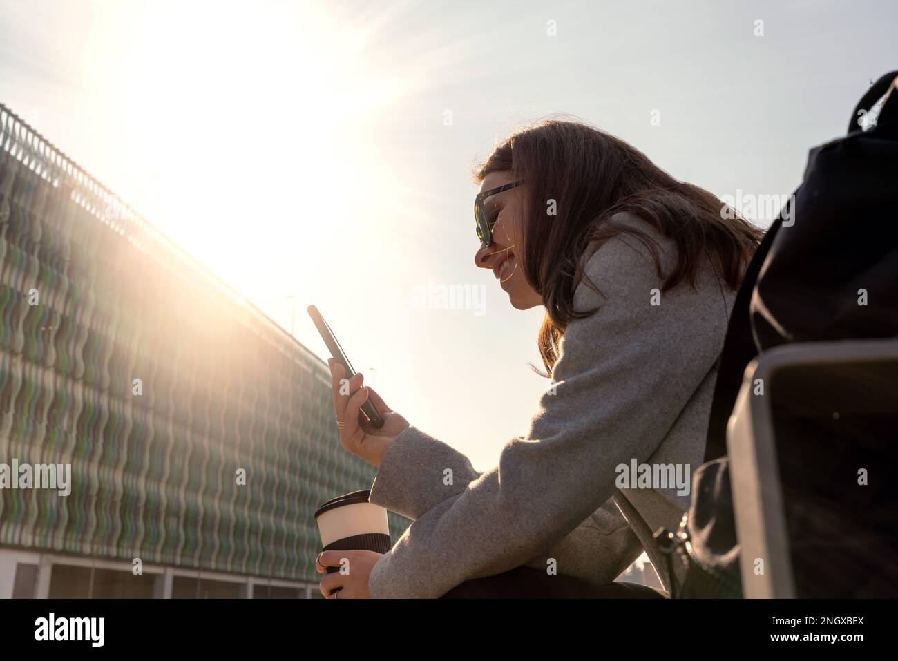 Jeune femme avec des lunettes de soleil assis sur le banc de rue et en utilisant son téléphone mobile messagerie en ligne. Banque D'Images