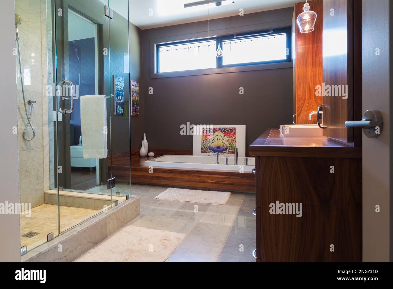 Meuble-lavabo en bois de noyer avec baignoire en acrylique blanc profond, cabine de douche en verre clair dans la salle de bains attenante avec sol en marbre gris et blanc à l'intérieur de la maison. Banque D'Images