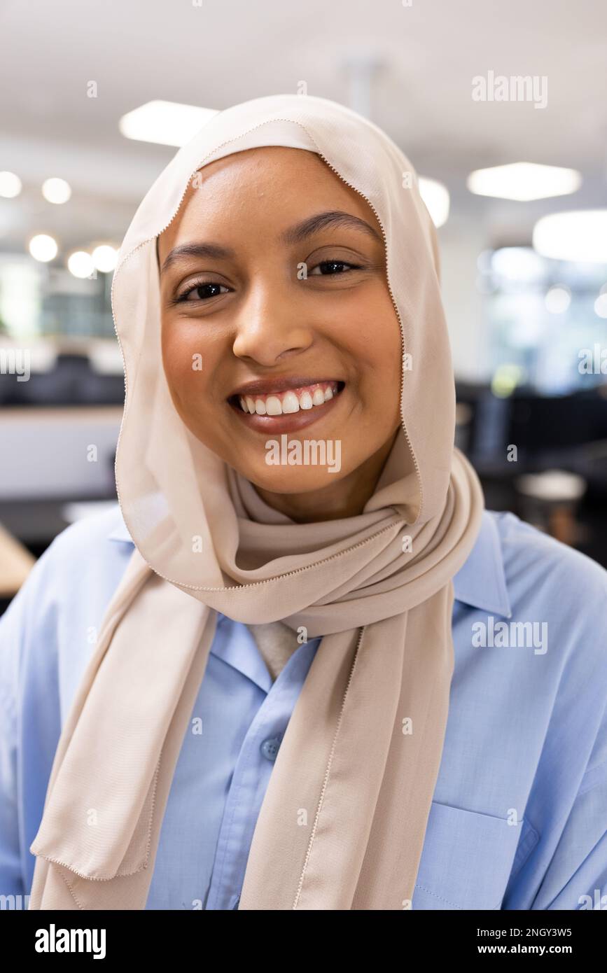 Image verticale d'une femme d'affaires du Moyen-Orient heureuse dans le hijab regardant la caméra dans le bureau Banque D'Images