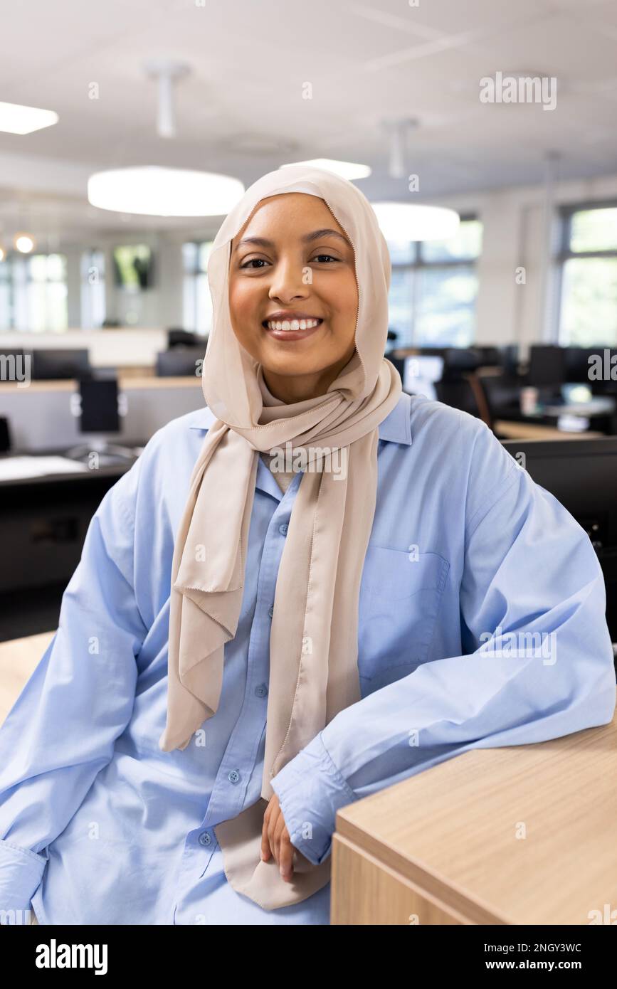 Image verticale d'une femme d'affaires du Moyen-Orient heureuse dans le hijab regardant la caméra dans le bureau Banque D'Images