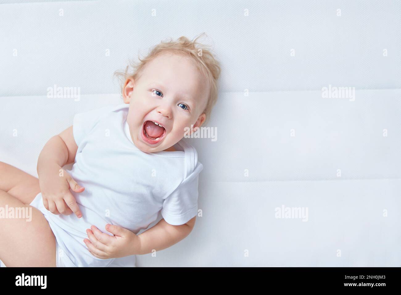 Portrait d'un enfant mignon.Amusant heureux rire bébé sur un matelas blanc dans la chambre blanche.Textile et literie pour enfants.Enfant regardant dans l'appareil photo.Heureux Banque D'Images
