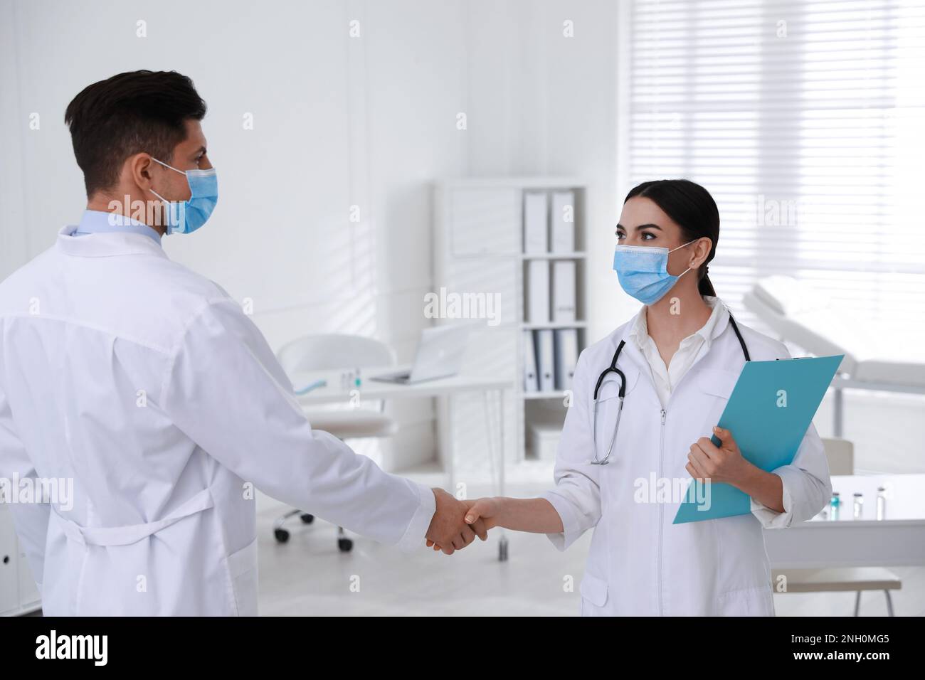 Médecins avec des masques de protection donnant poignée de main en clinique Banque D'Images