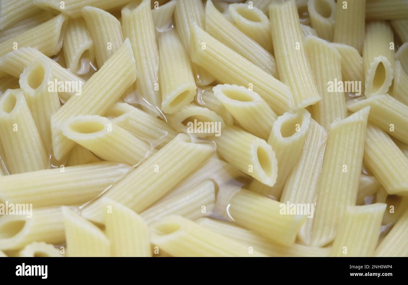 Nourriture et cuisine, Penne Pasta dans l'eau chaude, Une variété de pâtes italiennes en forme de tube, parfait pour divers plats avec sauces et ingrédients. Banque D'Images