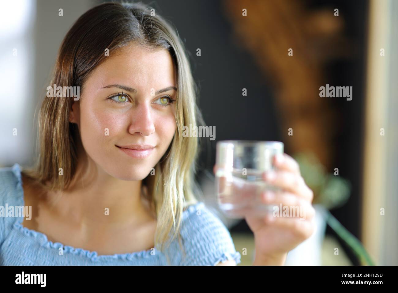 Bonne adolescente tenant un verre d'eau en regardant loin à la maison ou au restaurant Banque D'Images