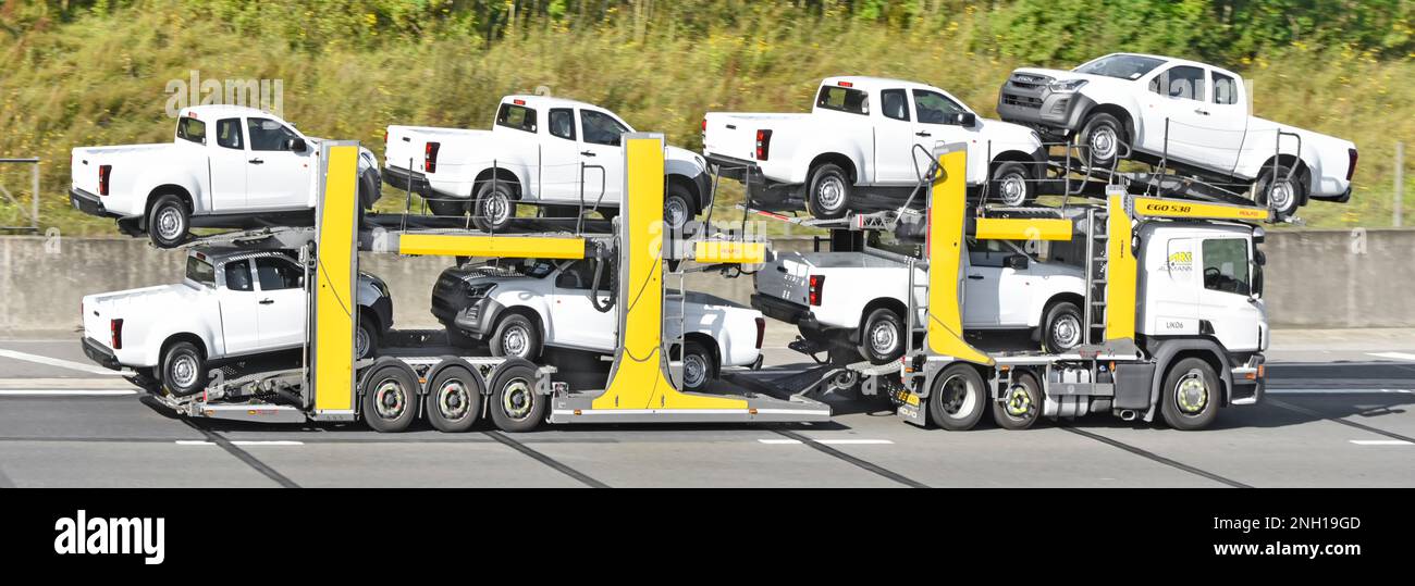 Sept pick-up blancs Isuzu chargés sur une remorque de transport de véhicule de voiture réglable et flexible remorqués par un camion hgv roulant sur la route autoroutière britannique Banque D'Images