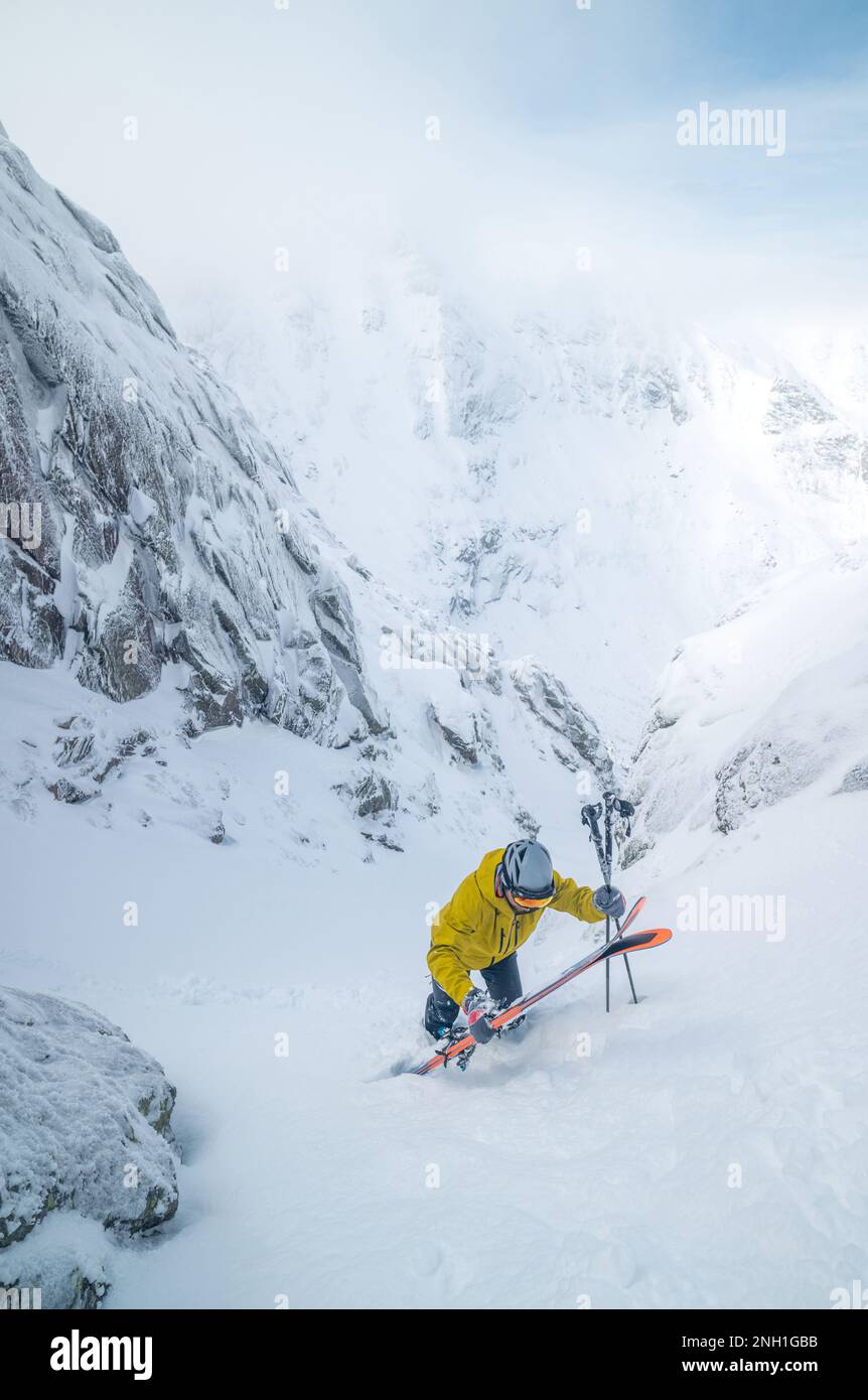 Skieur en blouson jaune remontant jusqu'au sommet de la piste de ski Banque D'Images
