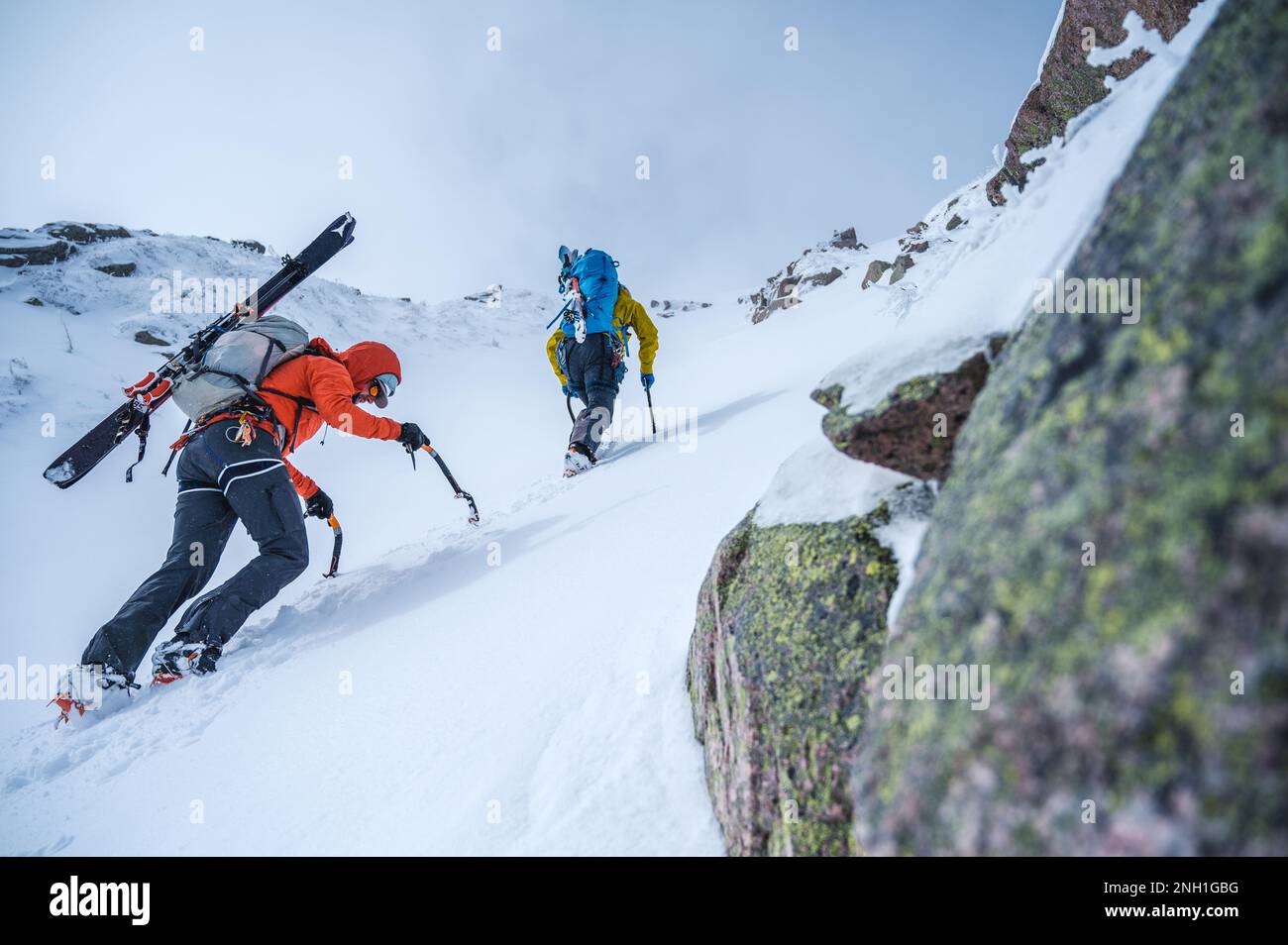 Deux hommes grimpent sur une ravin de neige raide avec des skis Banque D'Images