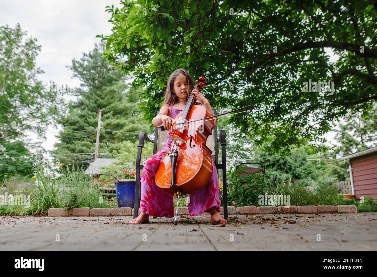Un petit enfant joue au violoncelle pieds nus dans le jardin sur le patio Banque D'Images
