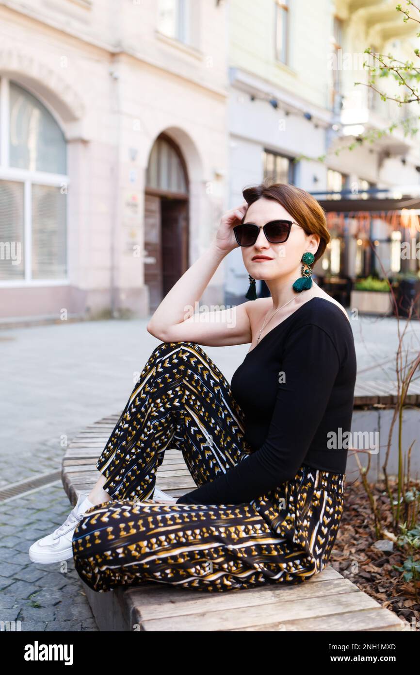 jeune femme élégante en lunettes assise sur une allée de ville en été Banque D'Images