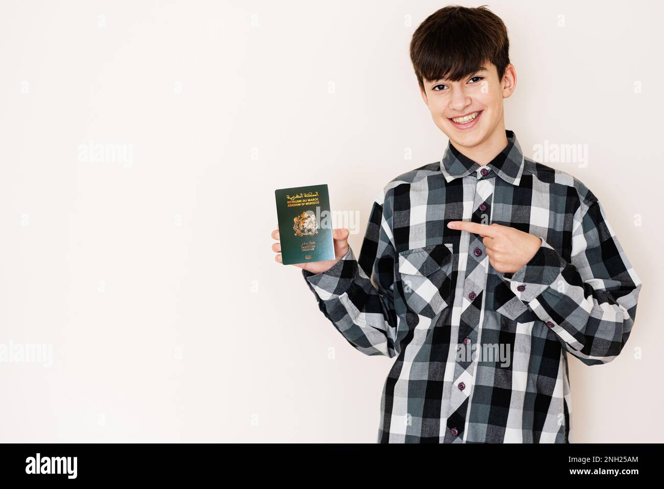 Jeune adolescent portant le passeport marocain, à l'aspect positif et heureux debout et souriant avec un sourire confiant sur fond blanc. Banque D'Images