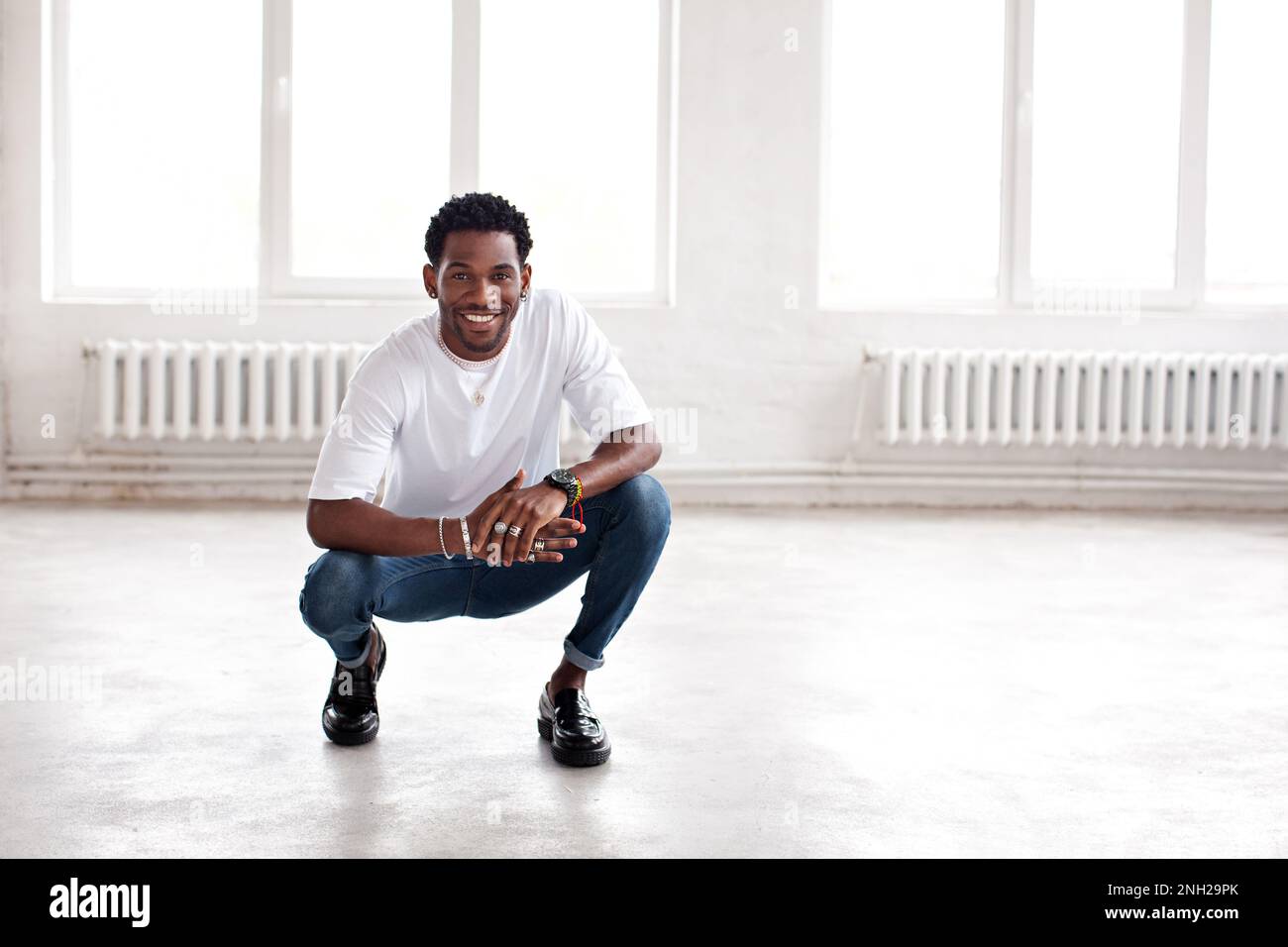 Beau homme heureux assis dans le loft intérieur, souriant. Cool hippster afro-américain gars Banque D'Images