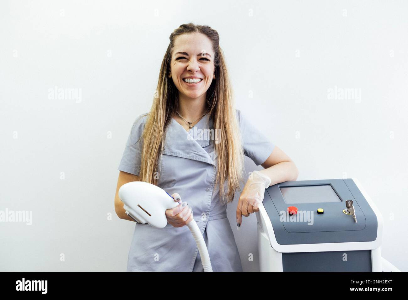 Jolie jeune femme dans un salon de beauté spécial uniforme et gants transparents se tient à côté d'une machine professionnelle de photoépilation. Épilation E-LIGHT Banque D'Images